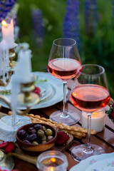 Beautiful romantic outdoor wedding decor in a field. Table decorated with purple lupines flowers. Wineglasses with white wine. Sunset, summer, golden hour. Perfect surprise date for loving couple