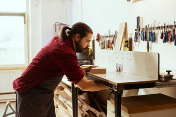 Man preparing wood shaper machinery, starting work on customer commissioned wooden objects in studio. Woodworker in carpentry shop installing spindle moulder equipment for manufacturing process