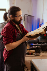 Cabinetmaker wearing safety glasses doing last touches on piece of wood before using it for furniture assembly. Woodworking expert doing inspection on timber block for damages