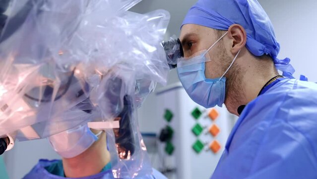 Concentrated bearded surgeon looks attentively at the microscope. Low angle view on the doctor working at neurosurgery.