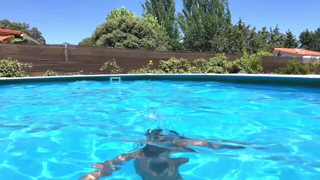 Video en c&aacute;mara lenta de un ni&ntilde;o feliz de 8 a&ntilde;os buceando y jugando en el agua de una piscina en verano, agua azul, sonriente y divertido