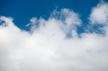 Small airplane flying in the clear blue sky with fluffy clouds