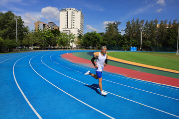 Fototapeta premium Senior Asian athlete is practicing running in the professional blue track for professional exercise, sport training workout and healthy for longevity concept