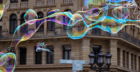 Many multicolored giant soap bubbles flying in the air on a windy day. Huge bubble are stretching on the wind into long smoothy changing form without popping. Close up. Copy space. Selective focus.