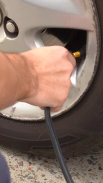 Primer plano de una mano inflando un neum&aacute;tico de autom&oacute;vil con una manguera de aire. Mantener la presi&oacute;n adecuada de los neum&aacute;ticos, esencial para la seguridad y eficiencia del veh&iacute;culo.