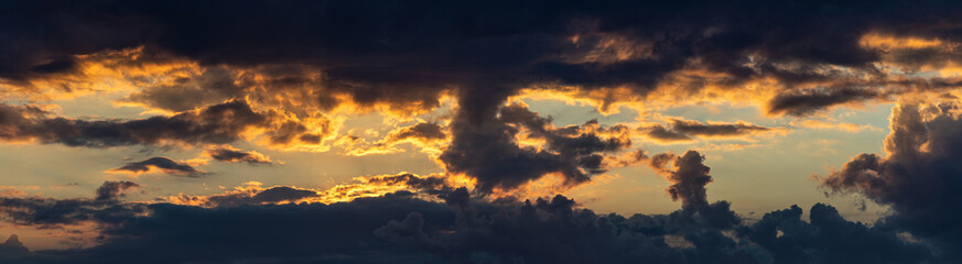 ampia composizione panoramica di immagini multiple dettagliate, che mostrano una vasta nuvola molto scura, in controluce, al tramonto, mentre il sole colora e crea sfumature di arancione nel cielo