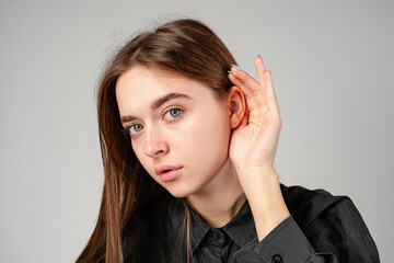 Young Woman in Black Shirt Listening Intently Against a Neutral Background.