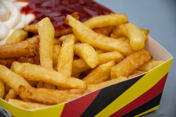 Belgian street and fast food, paper box in colors of Belgian flag with fried potato frit chips and ketchup and mayonnaise sauсe