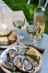 Plate with fresh live oysters with citron, bread, butter and white wine served at restaurant in oyster-farming village, Arcachon bay, Gujan-Mestras port, France