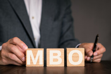 There is wood cube with the word MBO. It is an abbreviation for Management by Objectives as...