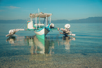 Traditional Filipino boat, known as a banca or bangka, is anchored on calm, clear sea waters. The...