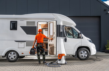Technician Cleaning a White Motorhome With a Vacuum and Repairing RV Appliances