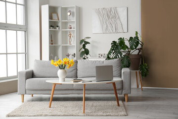 Interior of stylish living room with modern laptop and flower vase on coffee table