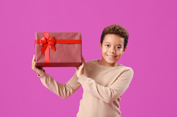 Little African-American boy with Christmas gift on purple background