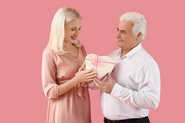 Happy mature couple with gift box on pink background