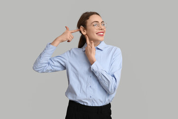 Beautiful young woman pointing at hearing aid on grey background