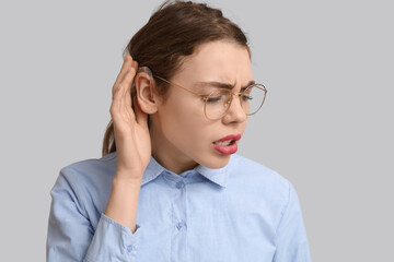 Beautiful young woman with hearing aid trying to hear something on grey background