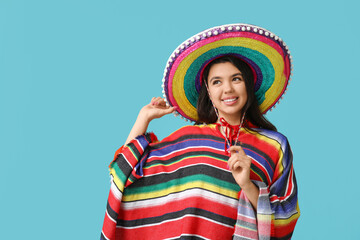 Beautiful young happy woman in poncho and sombrero on blue background. Cinco de Mayo celebration