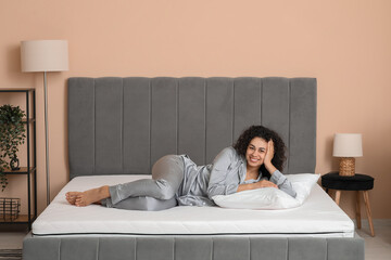 Obraz premium Young African-American woman with pillow lying on soft mattress in bedroom