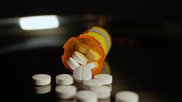 Prescription pills fall on the table from the bottle in slow motion. Pharmaceutical opioid painkillers crisis in America. Narcotic abuse adn addiction overdoses.  Macro close up shot.