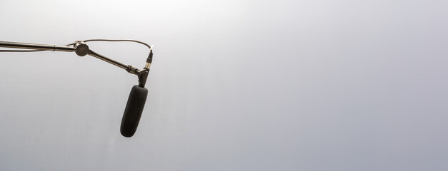 Simple black studio mic, microphone hanging placed on a long high top mic arm stand, plain gray...