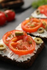 Delicious ricotta bruschettas with sliced tomatoes, olives and greens on black table, closeup