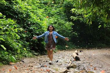 Naklejka premium A young lady wearing a short skirt with a butterfly print walks on the dirt road.There are swarms of butterflies along the way. Baan Krang Camp,KaengKrachan national park ,Phetchaburi,Thailand