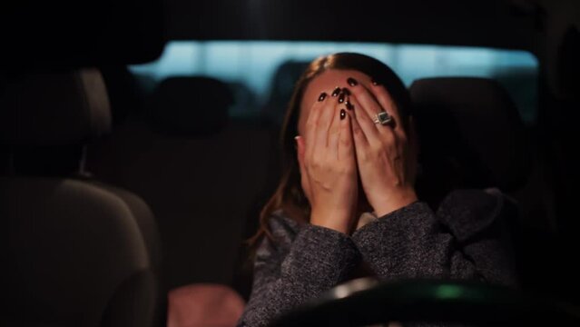 Portrait of woman sitting inside car in twilight, watching thriller, horror film in drive-in cinema, passions running high, peering closely, scared from surprise, covering eyes with hands, Reaction 