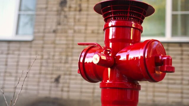 Close-up of red bright new fire hydrant mounted in the courtyard of a multi-story building, the metal flickers in the sun, slow motion from bottom to top Utility services fence city yards, fire safety