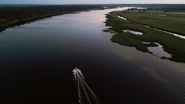 Aerial view of river with speedboat creating wake at sunset, capturing beauty of tranquil landscape