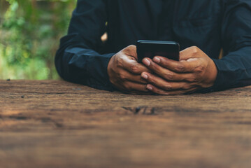 Close up Businessman hands using smartphone sitting at wood table in green garden. Man hands hoding...