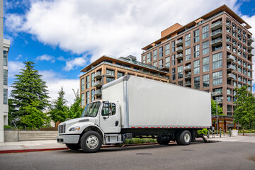 Compact powerful bonnet day cab middle duty rig semi truck carry goods in box tailer making delivery to customer in multilevel apartment