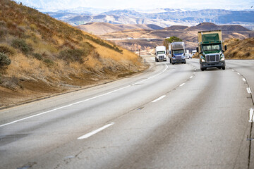 Convoy of the big rig semi trucks with semi trailers transporting cargo climbing on the wide...