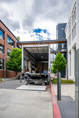 Local mover rig semi truck with long box trailer standing with open door and lowered lift on the city street making customer goods delivery
