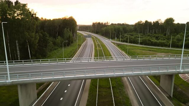 This is a serene image of an empty highway with an overpass at sunset, captured from an aerial perspective
