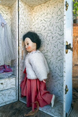 A female doll displayed in a store window gazes wistfully at a white lace gown