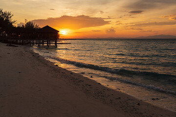 Sunrise silhouettes a dock and gazebo on a beautiful tropical beach