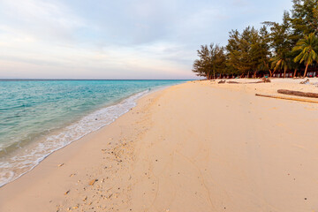 Beautiful remote tropical beach with white sand and sea shells in the blue and pink light of sunset