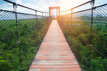 Obraz premium The sky bridge walkway above is a wooden staircase with sunlight. People walk or have the wind secretly swaying, it's exciting to see view or survey route of forest at Walailak University ,Thailand.