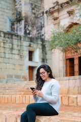 Latin woman using smartphone on church steps. Urban photography in Oaxaca, Mexico. Taken at Santo Domingo church. People and heritage concept.