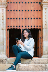 Latina woman using smartphone on church steps. Urban photography in Oaxaca, Mexico. Taken at Santo Domingo church. People and heritage concept.