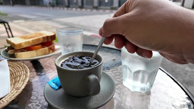 Hand holding tea spoon stiring coffee outdoor at cafe.