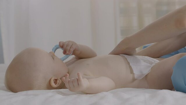 Infant boy during white diaper change, play with blue teether toy. Caregiver moment showcase parental love to child, comfort and attention in calm, soft lit environment, emphasize baby care essentials