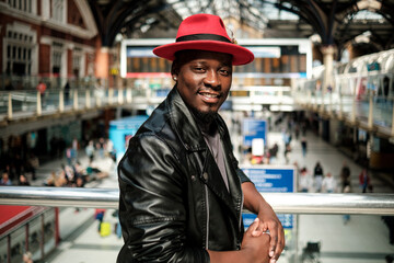 Happy black man posing in a train station leaning on a banister.