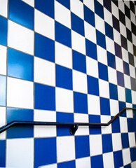 Vertical angled image of a blue and white checkered wall with a black handrail  in a stairwell