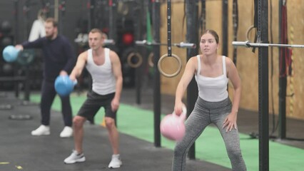 Attractive fit sporty young girl doing exercises with kettlebell to strengthen body muscles in modern gym during group workout. Physical activity and bodybuilding concept