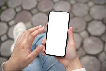 A close-up image of a woman using her smartphone while sitting outdoors.