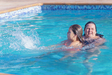 a mother holds her beautiful daughter in her arms teaching her to swim in the pool