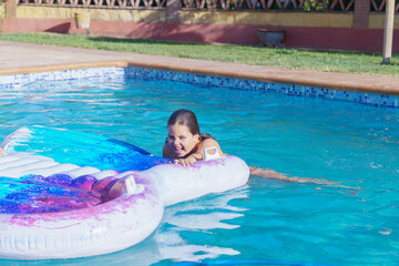 cute smiling girl climbing on an inflatable mattress at the pool