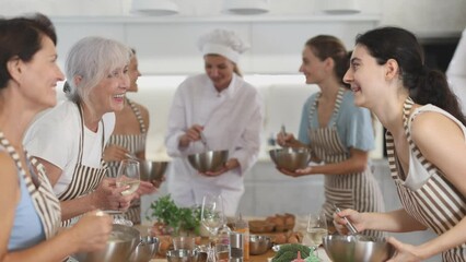  Elderly woman drinks wine and talks to group during cooking master class